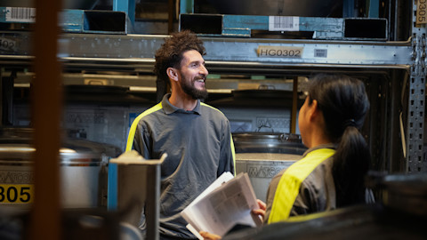 A man and a woman wearing work clothes facing each other in an industrial environment