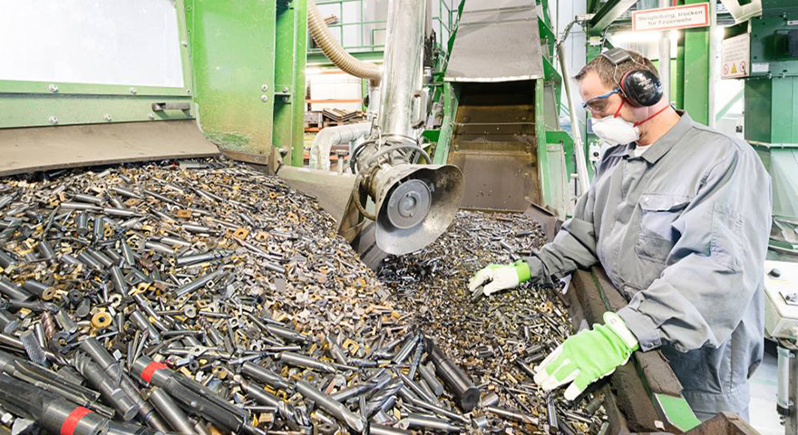 A man wearing personal protective equipment standing next to a big pile with used cemented carbide tools and inserts that are going to be recycled